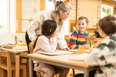 Pedagog står bakom två elever och pratar med dem