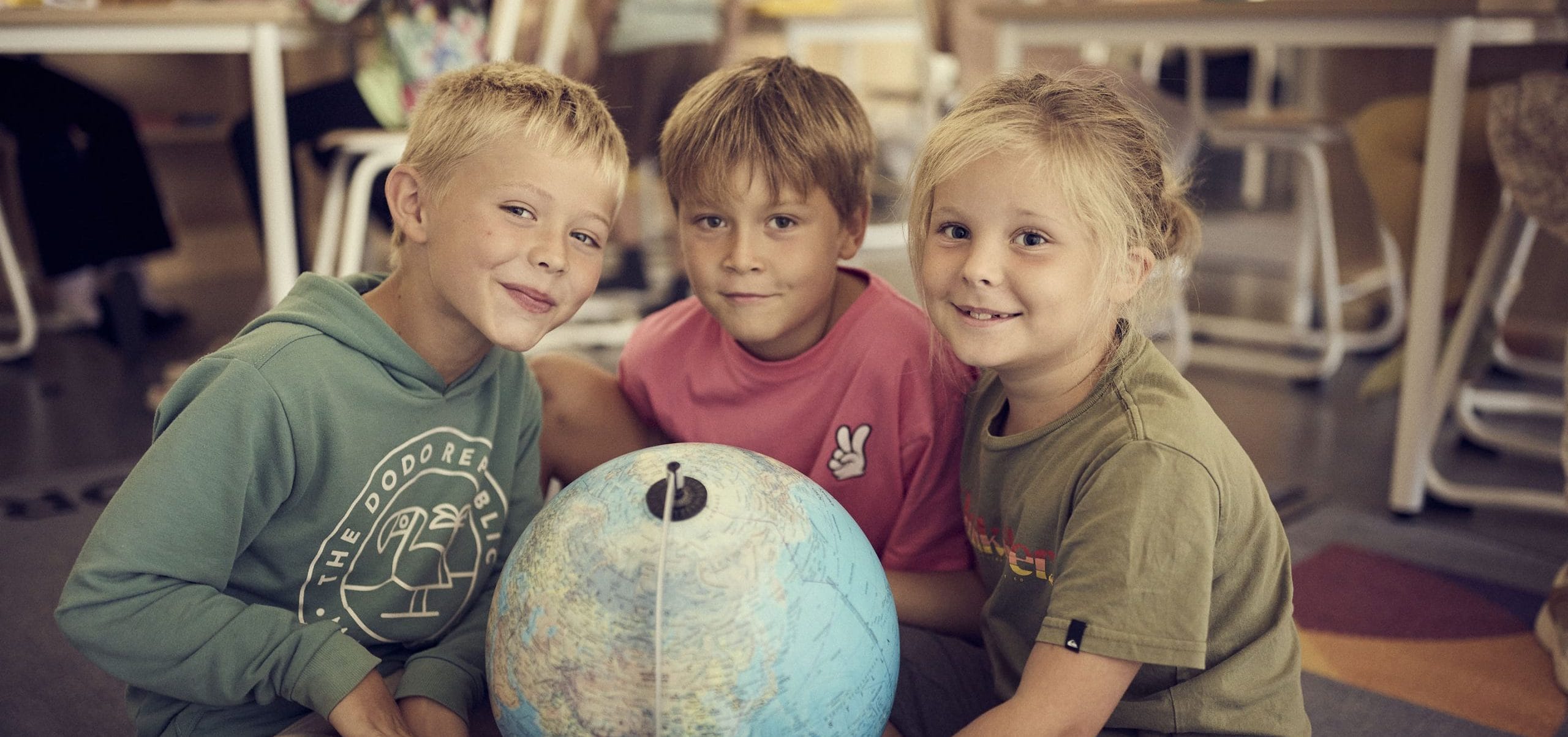 Tre elever på Montessori Mondial sitter på golvet med en jordglob.