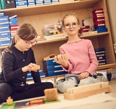 Två elever sitter på golvet och lär med montessorimaterial.