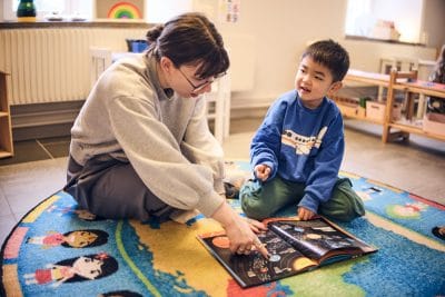 Barn och pedagog sitter på mattan och kollar i en bok över rymden.