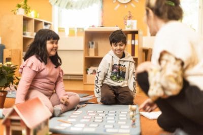 Två elever sitter på golvet tillsammans med en pedagog.