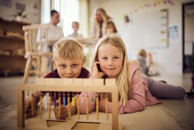 Två elever i förskoleklass ligger ner på golvet och lär med montessorimaterial.