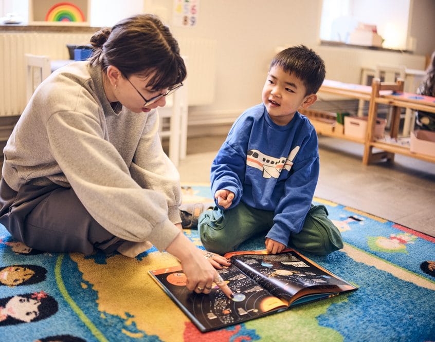 Pedagog och barn sitter på golvet och läser bok om rymden.