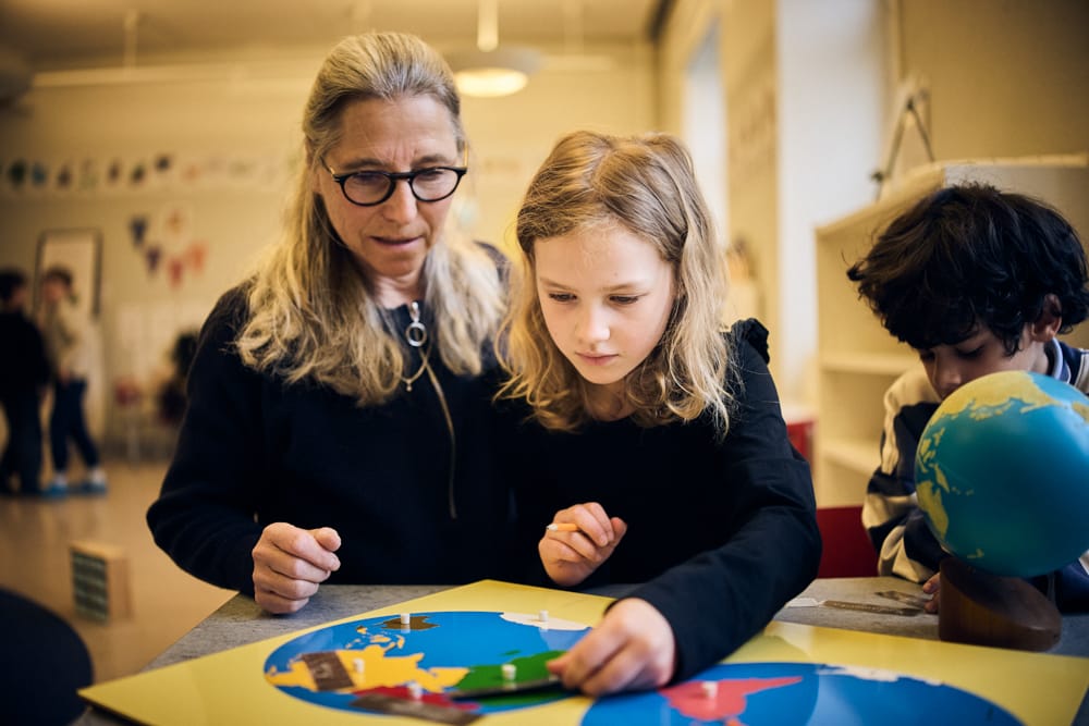 Elev lägger pussel föreställande världen tillsammans med pedagog.