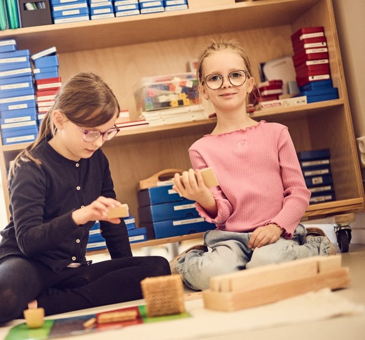 Två elever sitter på golvet och lär med montessorimaterial.