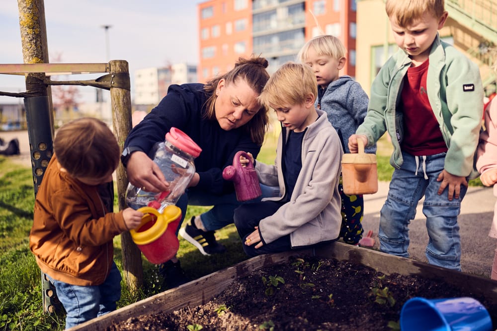 Förskolebarn får vatten i sina vattenkannor.