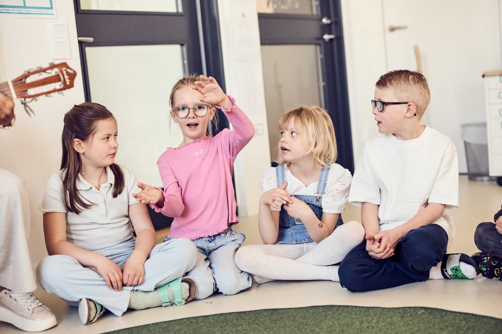 Eleverna sitter på golvet och lyssnar på en tjej som demonstrerar med händerna.