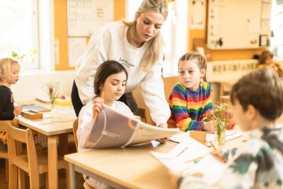 Pedagog står bakom två elever och hjälper den ena med skolarbete