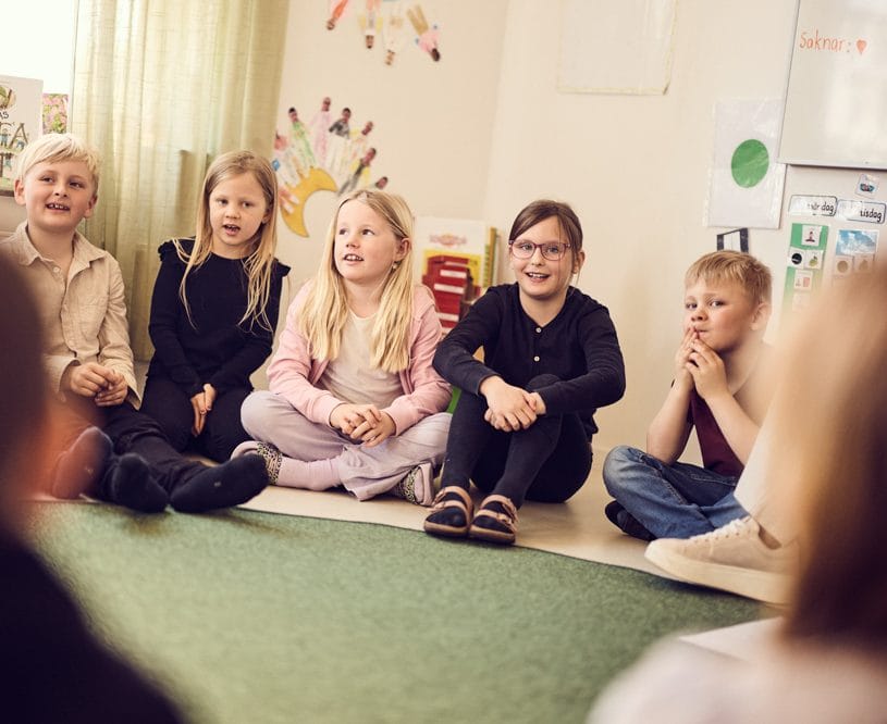 Flera elever sitter i ring på golvet och sjunger.
