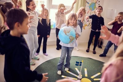 En elev i förskoleklass håller i en jordglob och klasskompisarna sjunger i en ring runt henne.