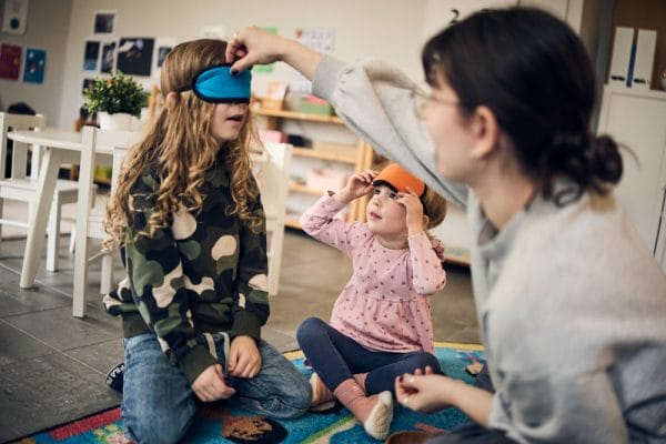 Två förskoleelever på Montessori Mondials förskola med pedagog som lär med ögonmask.