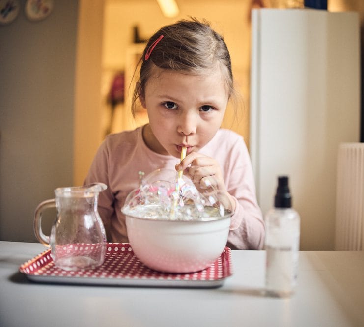 Förskolebarn bubblar genom sugrör.