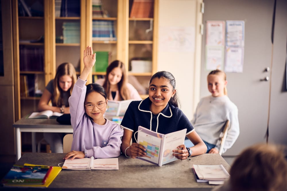Elever sitter i klassrum och en räcker upp handen.