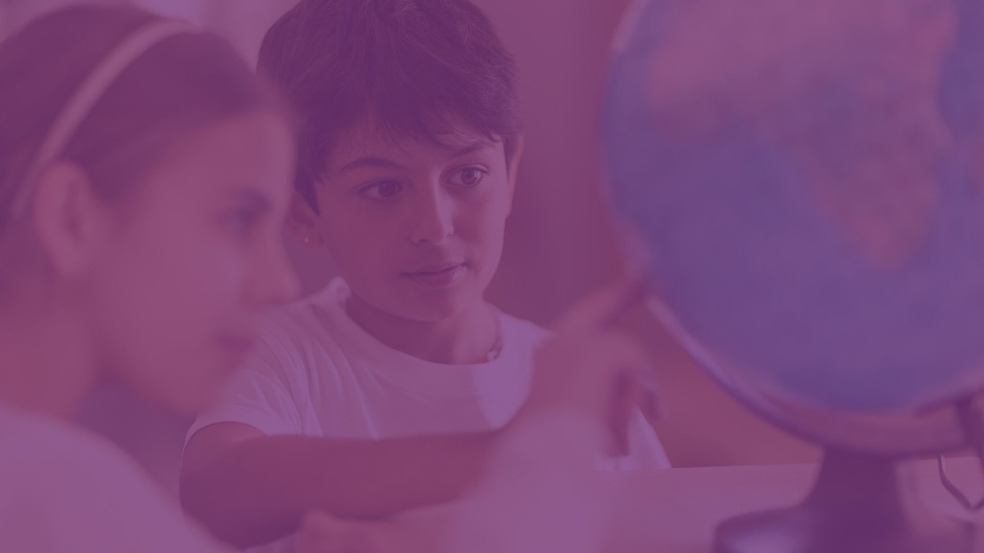 Två elever på Montessori Mondial Nacka sitter vid ett bord och tittar på en jordglob.