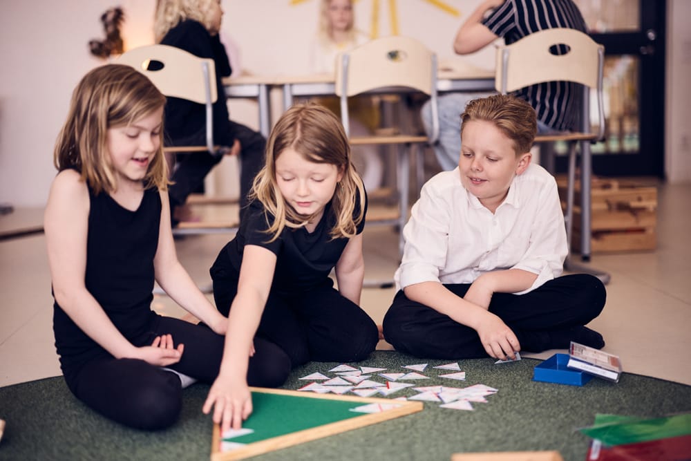 Tre elever sitter på golvet och lär med montessorimaterial.