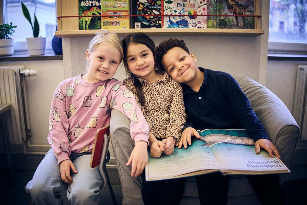 Tre förskoleklasselever läser böcker.
